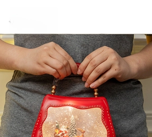 Close-up of a hand holding a glowing red Christmas snow globe lantern with Santa inside