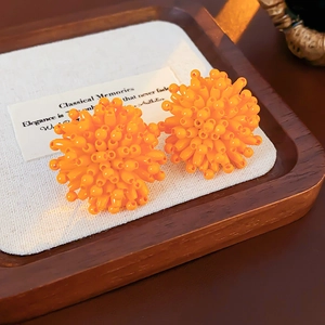 Macro shot of orange beaded cluster earrings on a vintage wooden tray with fabric