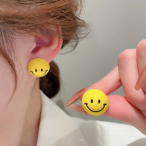 Close-up of cute yellow smiley face earrings with silver needle shown on ear