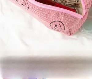 Detail of pink corduroy makeup pouch with a smile pattern holding beauty tools
