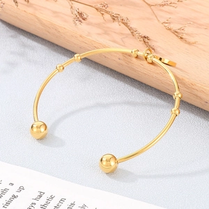 Detail of 18K gold-plated open bangle with sphere charms and glossy metal texture