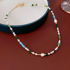Detail view of pearl and multi-color beaded necklace with golden T-bar clasp on red leather