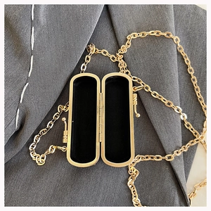 Detail of golden rectangular chain bag with black lining on a grey blazer