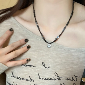 Close-up of black beaded necklace with silver bamboo lock pendant on a person's neck