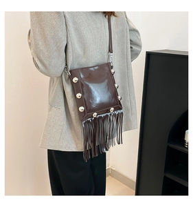 Detail view of dark brown tassel crossbody bag with shiny finish and silver studs