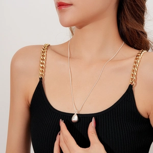 Gros plan d'un pendentif goutte en argent mat sur une chaîne fine portée par une femme