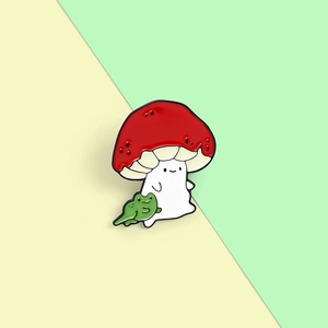 Detail view of cartoon red mushroom with smiling face holding a green frog enamel pin