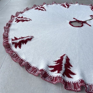 Detail of white knitted Christmas tree skirt with red cedar patterns and tassel trim