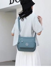 Macro view of blue nylon crossbody bag with multiple zippers and round logo detail