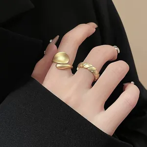 Detail of matte gold oval pea ring and twisted rope band worn on hand against black suit
