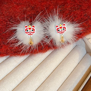 Detailed close-up of white fluffy dancing lion earrings with gold bells on red velvet