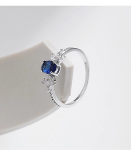 Detailed close-up of oval blue sapphire ring with teardrop diamonds on a white stand