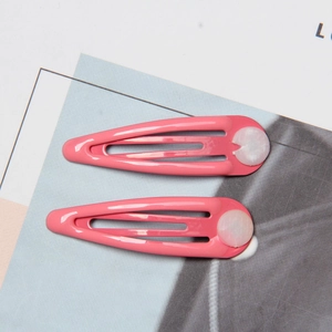 Detail of two pink metal drip hair clips with white decorative elements on paper