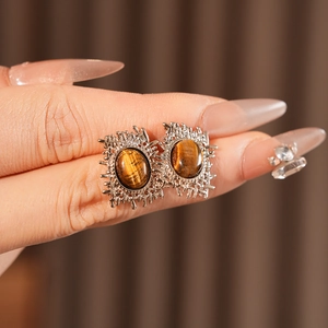 Detail shot of vintage silver-tone earrings featuring oval tiger eye stones in hand