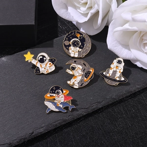 Detailed set of astronaut enamel pins with whale and moon motifs on a stone surface