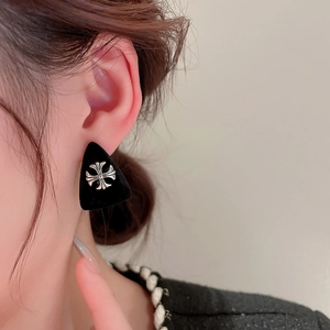 Detail of vintage black triangle earring with silver cross floral emblem on model