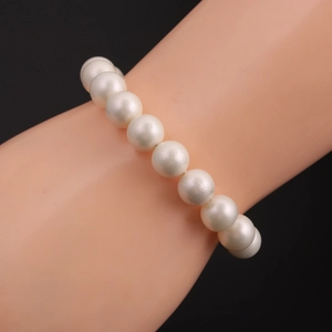 Close-up of a classic white pearl bracelet worn on a wrist against a black background