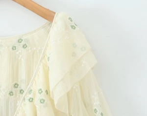 Dettaglio del ricamo floreale e delle balze su un abito beige con scollo a V