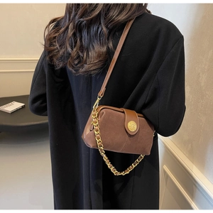 Detail of a brown suede crossbody bag featuring a golden lion head buckle and chain
