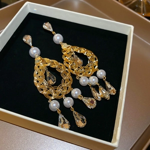 Detail of gold flower petal earrings with woven circle, pearls, and crystal drop charms