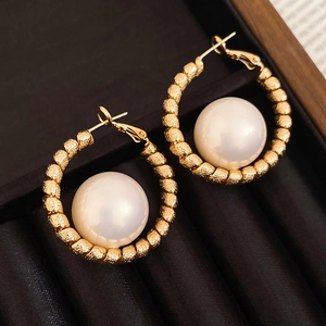 Close-up of gold textured hoop earrings featuring large white pearls on black velvet background