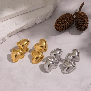 Polished gold and silver heart stud earrings on a textured stone display