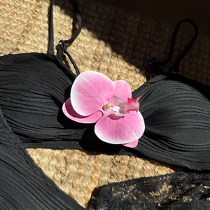 Close-up of black textured bikini top with a pink orchid flower on straw mat background