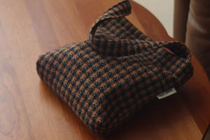 Detailed view of houndstooth plaid wool fabric and brand label on small handbag