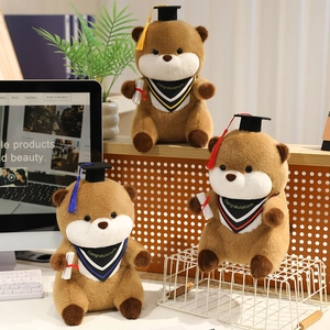 Three plush graduation otters with mortarboards and diplomas on a desk setting