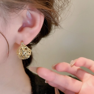 Close-up of golden earrings featuring intricate hollow coral texture on a female model