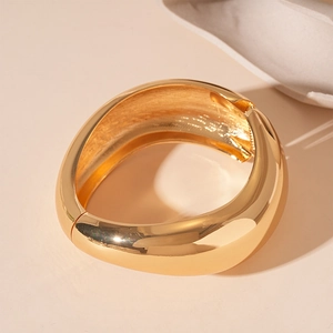 Macro detail of glossy gold metallic wide open cuff bracelet with irregular distorted texture
