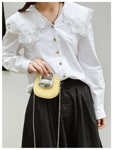 Close-up of a mini yellow saddle bag with silver metal handle and chain strap on a model