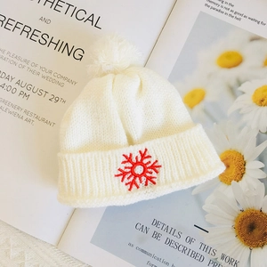 Detailed view of a white knitted hat with a red snowflake pattern and pom-pom for dolls