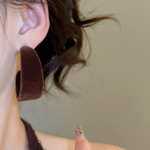 Gros plan d'une boucle d'oreille créole en forme de C floquée marron sur un modèle