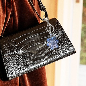 Blue crystal flower keychain accessory shown hanging on a dark crocodile leather handbag