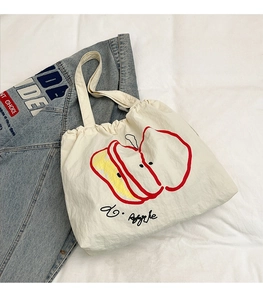 Flat lay of a white canvas tote bag with artistic red apple print and yellow detail