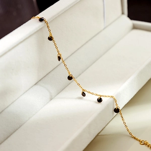 Detailed close-up of a minimalist gold bracelet with black circular charms on white velvet