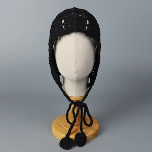 Détail d'un bonnet au crochet noir avec motifs ajourés et longues lanières à glands