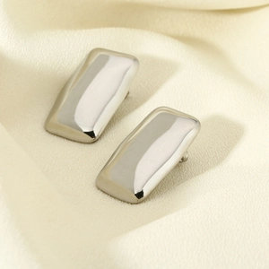 Detailed close-up of polished silver rectangular stud earrings on white silk fabric