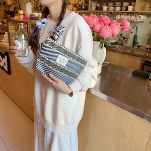 Detailed close-up of woven striped makeup bag with colorful logo tag in hand