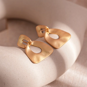 Macro detail of matte gold irregular geometric earrings with textured metal finish