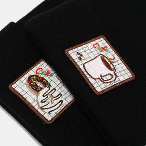 Close-up of donut and coffee cup embroidery patches on a black knitted beanie cap