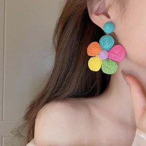 Detailed view of colorful woven flower earrings with vibrant raffia texture on model