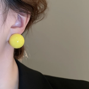 Close-up of a model wearing bright yellow spherical stud earrings with a glossy finish