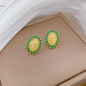 Close-up of golden oval earrings with green gemstones and religious relief details