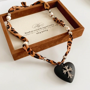 Detail of leopard print fabric necklace with black heart cross pendant in a wooden box