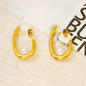 Vue détaillée d'une boucle d'oreille dorée en U avec une perle blanche sur texture
