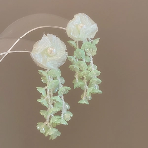 Close-up of chiffon flower earrings with pearls and green tassel beads on clear stand