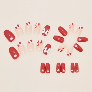 Detail of press-on nails with red heart patterns and 3D bows on a neutral background