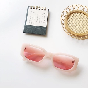 Detail view of pink thick frame sunglasses with red lenses on a minimalist desk setup